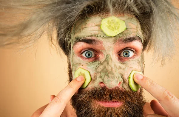 Funny face of man applying cucumber slices over clay mask, temper morning spa procedure, close up