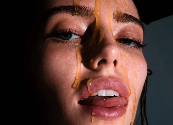 Portrait of young woman. Beautiful girl tongue licking honey lips. Sensual young woman face with honey drop close up. Sexy model with honey drip on face