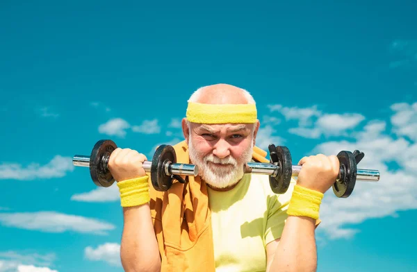 Old sportman exercising with lifting dumbbell on blue sky background. Isolated, copy space