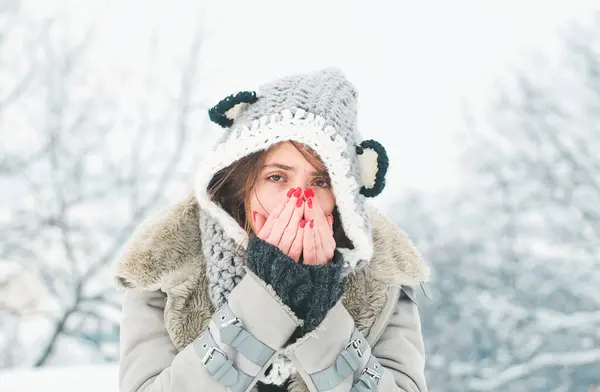 Young woman with nose wiper near winter tree. Woman with napkin sneezing in the winter snowy park. Young woman having flu and blowing her nose