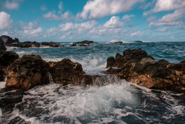 Deniz taşlarla ve kumsalın kumuyla çarpışıyor. Deniz dalgaları taşa çarpıyor.