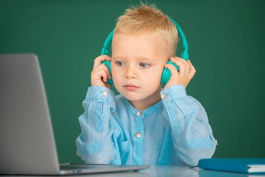 Kulaklık takan küçük bir çocuk okulda bilgisayar dersleri alıyor, kulaklık takan bir çocuk internetten bilgisayar kullanıyor..