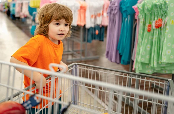 Boy grocery shopping at the supermarket sitting in the cart helping his mother. Funny child with shopping trolley with in grocery store