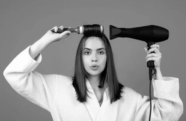 Woman combing hair. Portrait of female model with hair dryer. Girl with hairbrush, hair care and beauty. Morning routine