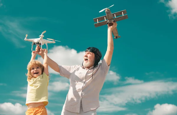 Grandson child and grandfather playing with toy plane and quadcopter drone against sky. Child pilot aviator with plane dreams of traveling. Family Relationship Grandfather and child