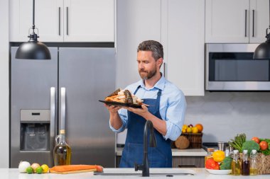 Mutfakta çiğ somon filetosu olan şef önlüklü adam. Üniformalı şef mutfakta önlük pişiriyor. Şef şapkalı yakışıklı şef mutfakta çiğ balık fileto pişiriyor.