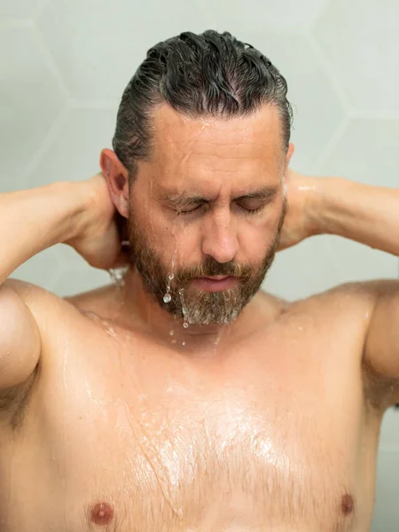 Man washing hair, closeup portrait. Bathing shower washing hair head in bathroom. Male model washing hairs in shower. Man taking shower. Guy showering, hair care. Male shampoo and washing hair concept