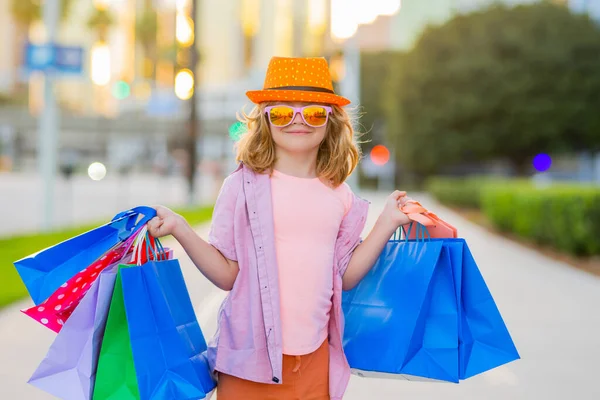 Cute shopper. Child with many shopping bags outdoor. Cute little boy in fashion kids clothes with shopping bags walking on street. Black friday and discount, sale