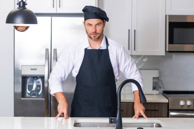 Mutfakta şef üniforması giyen yakışıklı orta yaşlı bir adam. Aşçılık ve aşçılık. Restoran menüsü konsepti. Yemek servisi, yemek pişirme, yemek reklamcılığı. Üniformalı adam mutfakta.
