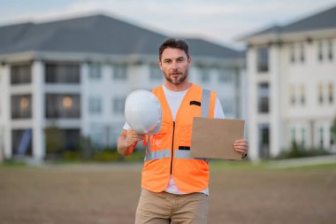 Mühendis kâğıt tahtasını metin için tutuyor. Tabelacı pankart afişi ve poster gösteriyor. İnşaat alanında çalışan biri. İnşaat müdürü ya da mühendis dışarıda kask takıyor. Erkek inşaat mühendisi
