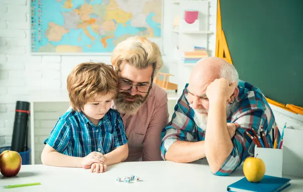 Grandfather and father teaching son. Granddad and cute little boy grandson study and learn together, playing games. Senior grandpa and middle aged dad play with grandchild son