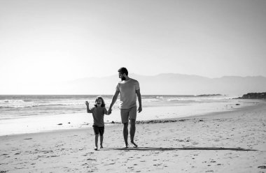 Baba ve oğul yaz plajında yürüyor. Baba ve çocuk dışarıda oynuyorlar.