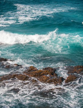 Denizde kayaların üzerine dalgalar sıçrıyor. Dalga okyanustaki taşa su borusuyla vurdu.