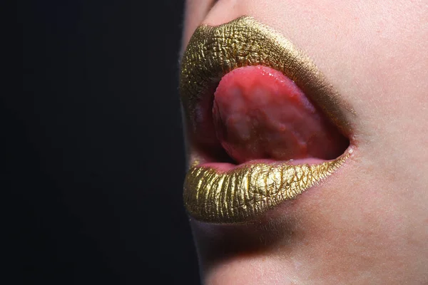 Sexy tongue licking lips. Golden lips. Luxury gold lips make-up. Golden lips with creative metallic lipstick. Gold metal lip. Sensual woman mouth, clse up, macro