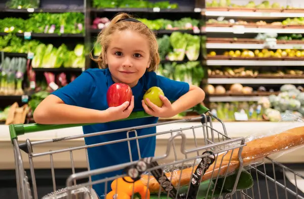 Kid with apple fruits at grocery store. Shopping with kids. Kid buying fruit in supermarket. Little boy buy fresh vegetables in grocery store. Kid choosing vegetables. Healthy food