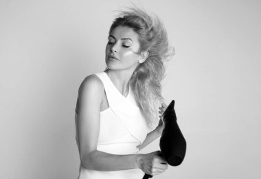 Saç kurutma makineli, gülen sarışın bir kadın. Saçlarını kurutan kız.