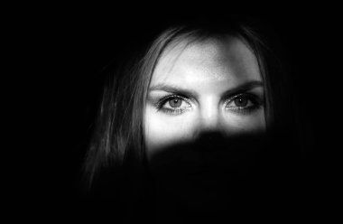 Şehvetli kız yüzü gölgede kaldı. Siyah arka planda ışığı olan zarif bir kadın. Güzel kadın vücudu. Mavi gözlü, ciddi bir kadın.