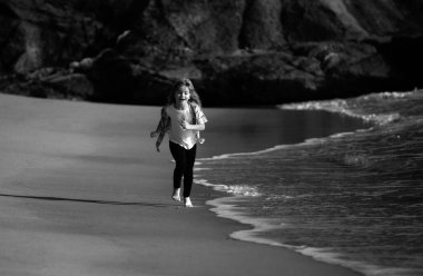 Sahilde oynayan çocuklar. Çocuklar yaz tatilinde denizde oynarlar. Kum ve su eğlencesi, güneş koruması. Eğitimdeki küçük bir atlet. Koşucu spor yapıyor, çocuklar için koşuyor.