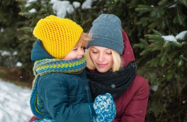 Anne ve oğlu kışın tadını çıkarıyorlar. Çam ağaçları karla kaplı. Güzel bir aile kışın karlı ormanda yürüyor. Tatiller, Noel, birlikte mutluluk, aşkta çocukluk.