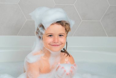 Çocuklar banyo yapıyor. Şampuan köpüğü ve banyo yapan saçlarında kabarcıklar olan bir çocuk. Köpüklü çocuk suratı, saç bakımı ve hijyen konsepti. Çocuklar uzun saçlar için şampuan kullanırlar. Banyoda saç yıkamak.