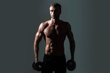 Seksi spor gövdesi, dambılı adam. Dambılı bir sporcunun portresi. Stüdyoda kaslı, gömleksiz bir adam var.
