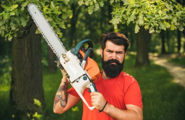 Ciddi yüzdeki oduncu elektrikli testere taşır. Ormanların tahrip edilmesi doğal ekosistemlerin bozulması ve istikrarsızlaşmasının başlıca nedenlerinden biridir. Adam işini yapıyor.