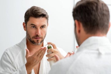 Amerikalı bir adam kırışıklığa yüz kremi sürüyor. Sabah güzellik rutini. Kırışık derili bir adam. Yaşlanma önleyici ve kırışıklık önleyici krem. Erkek güzelliği kavramı. Kırışık cilde krem süren adamın yüzünü kapat.