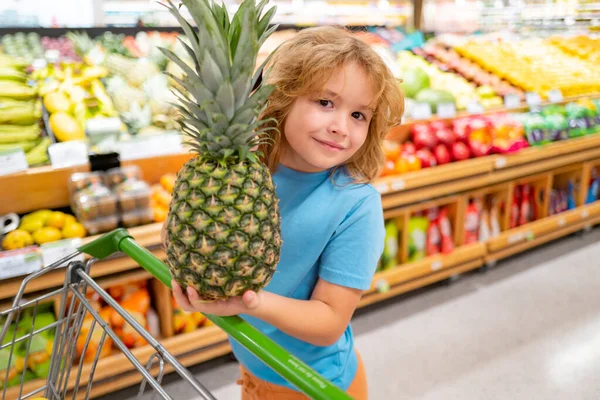 Happy little kid with fruits and vegetables at grocery store. Healthy food for young family with kids. Happy child with shopping cart full of fresh vegetables. Kids at grocery store or supermarket