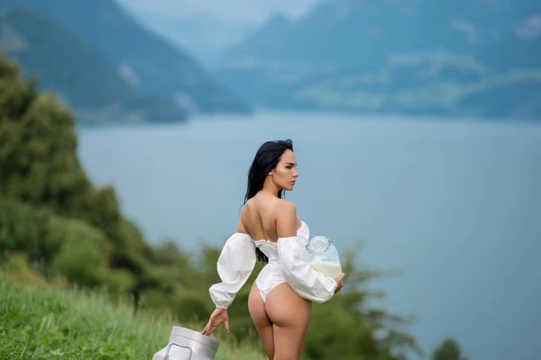 Milk concept. Sexy woman in lingerie outdoor. Sexy brunette woman with milk in Switzerland Alps. Alpine country girl. Bottle of raw milk against Alpine countryside. Sexy woman with milk in Alps