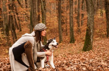Şapkalı, uzun gri kazaklı ve köpeğiyle oynayan alımlı, çekici bir kadın. Evcil hayvanı dışarıda dinlenen bir kız. Sonbahar hafta sonu. Sonbahar modeli