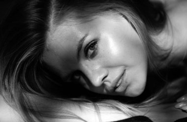 Çekici ve şehvetli görünen güzel kadın modelinin portresi. Sarışın, gülümseyen, yakından bakan kız. Siyaha izole edilmiş dramatik stüdyo ışığı olan güzel bir yüz.