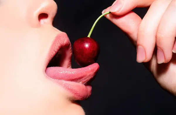 Cherry in woman mouth. Cherries on woman lips. Tongue lick cherry, macro, close up. Sexy tongue