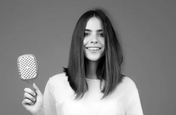 Girl combing hair. Beautiful young woman holding comb straightened hair