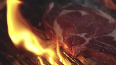 Izgara biftek. Yemek ve yemek. Yanan ızgarada biftek pişiyor. Izgara biftek. Kızarmış mermer biftek ateşte. Izgarada alevli biftek var. Barbekü ve ızgara. Biftek.
