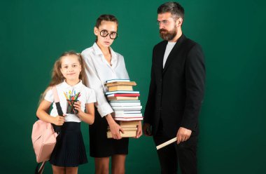 Baba, öğretmen ve okul çocuklarının portresi yeşil karatahta arka planda. Kitap okumak ve yazmak. Babam okulda kız öğrencilere ders veriyor.