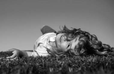 Çocuk yeşil çimlerin üzerinde yatıyor. Mutlu çocuk yeşil bahar tarlasında gökyüzü arka planına karşı oynuyor. Özgürlük çocukları ve hayal gücü kavramı