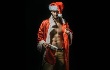 Noel seksi adam. Noel Baba şapkalı güçlü adam. Yeni yıl şeritleri ve yetişkinler için hediyeler. Noel 'de kas geyliği. Kaslı vücutlu Noel Baba. Siyah arka planda seksi genç Noel Baba