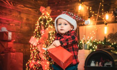 Mutlu Noeller ve mutlu Noeller. Komik bebek, Noel arkaplanında elinde bir Noel hediyesi açıyor. Noel ağacı. Mutlu çocuk.