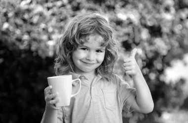 Fincanlı şirin çocuk portresi, elinde bitki çayıyla büyük bir bardak tutan çocuk. Mutlu çocukluk