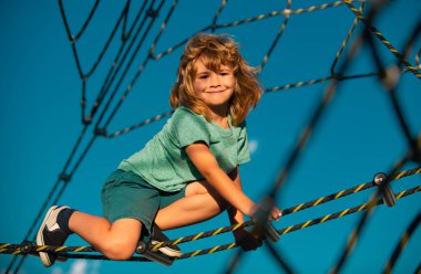 Oyun parkında ağlara tırmanan sevimli, gülümseyen çocuk. Çocuklar ip parkı. Komik çocuk suratı