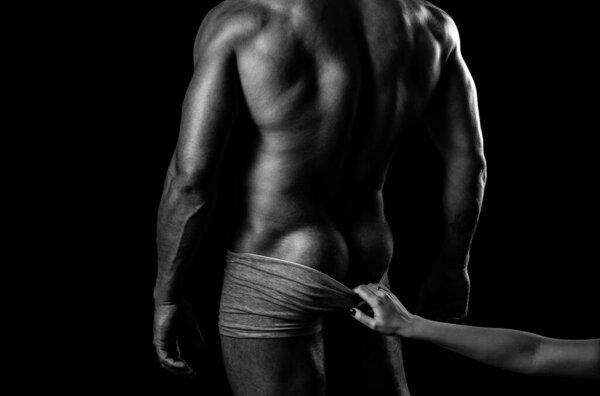 Shirtless athletic man turned back on black background. Masculine buttocks. Sexy provocative fashion portrait of young hot naked guy