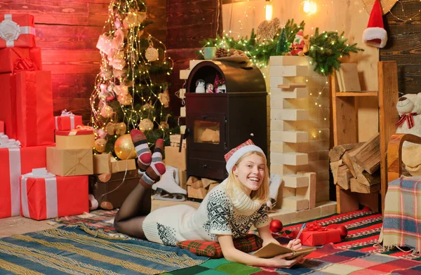 クリスマスの魔法の概念 家族と一緒に居心地の良い装飾された家で幸せな冬の休日 若いですブロンド女の子で編んだセータードレスと赤い帽子書きますザ プレゼントのリストへサンタ — ストック写真