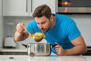 Evde yemek pişirmek. Mutfakta yemek hazırlayan adam. Erkek aşçı evde yemek hazırlıyor. Şef yemek yapıyor. Yemek pişiren adam, mutfak tenceresi, yemek tabağı. Adam mutfak içinde çorba hazırlıyor.