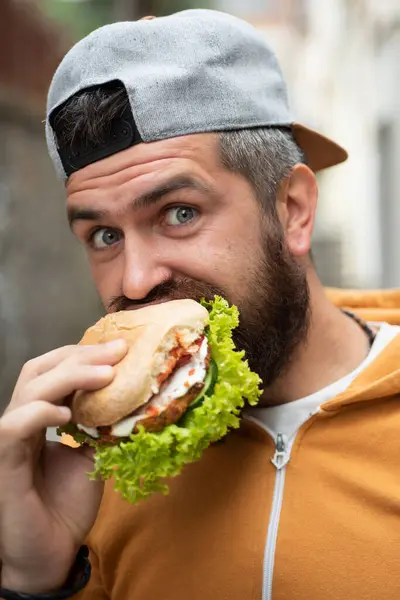 Hunger Man eat Hamburger outdoor. Man eat tasty Hamburger on street. Burger on lunch. Cheeseburger or hamburger. Man eating tasty Hamburger outside. Tasty take away Hamburgers