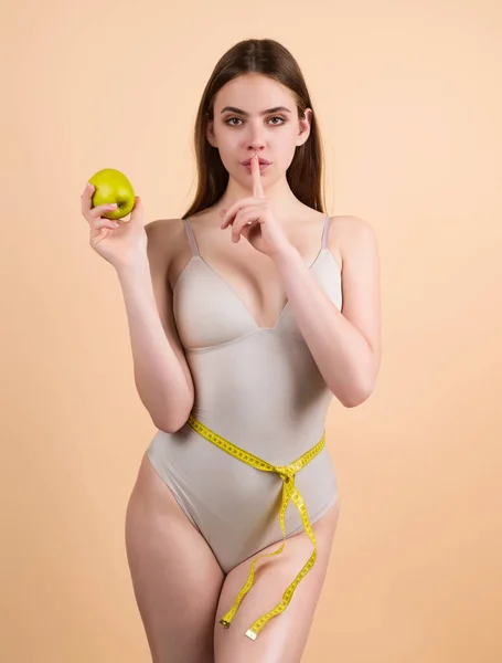Young woman measuring waist. Weight loss for slim waist. Female model with slim waist holding apple and measuring tape. Weight loss and dieting. Exercise for waistline. Fit Body. Waist and belly