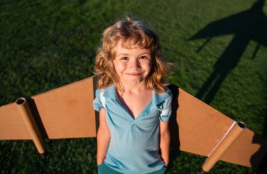 Sırt çantalı kanatlı bir çocuğun portresi. Pilot pilotçuluk oynayan ve dışarıda parkta rüya gören bir çocuk. Gülümseyen çocuk yaz tatili ve seyahat hayali kuruyor.