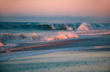 Tropikal denizin üzerinde sahil gündoğumu. Sahilde dalgaların sıçradığı renkli bir gün batımı. Okyanus dalgaları arka planı