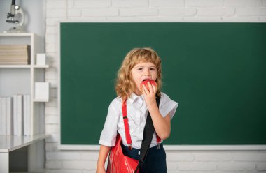 Sınıfta elma yiyen küçük bir öğrenci, okulda İngilizce öğreniyor. Dahi çocuk, bilgi günü