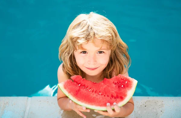 子供は夏休みにプールの近くでスイカを食べる 子供たちは屋外で果物を食べる 子供のための健康食品 小さな男の子のプールで水メロンのスライスで遊んで — ストック写真