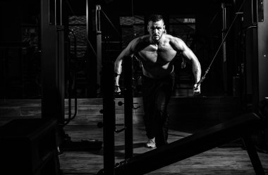Kaslı ve güçlü adam egzersiz yapıyor. Güçlü kaslı adam spor salonundaki egzersizleri yukarı itiyor, trisepslerde egzersiz yapıyor. Sporcu ağırlıklarla egzersiz yapıyor. Fitness ve Crossfit